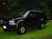 2000 Chevrolet Blazer - This black SUV is parked on a grassy lawn with trees behind it. A watermark indicates the year 2000.