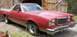 1977 Ford Ranchero - This red pickup truck has a distinctive grille and body style, parked outside a barn-like structure.