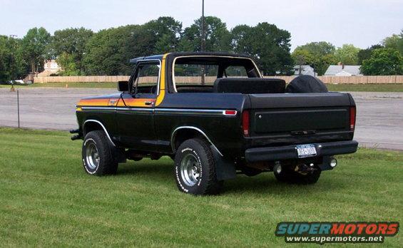 Black Ford Bronco with orange and yellow stripe on the side. It has a removable top and a spare tire in the bed