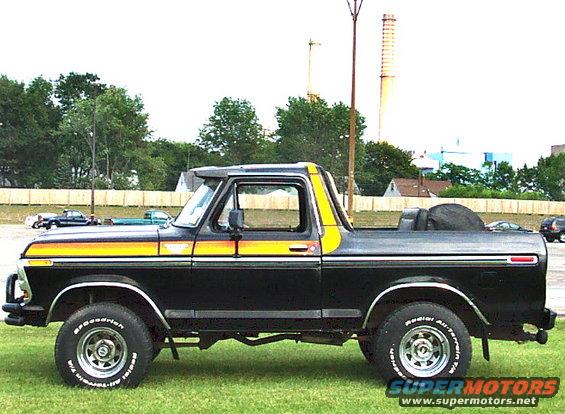 Black 1978 Ford Bronco with yellow and orange side stripes, parked on grass