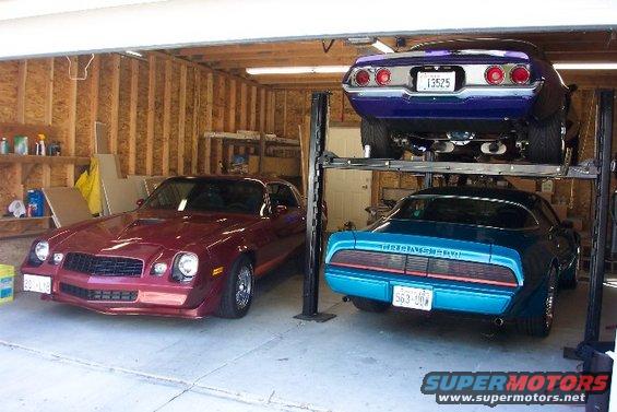 Maroon car on left, blue Trans Am in middle, purple car on lift. Garage setting