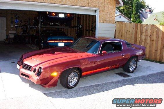 Red coupe with orange stripe, chrome wheels, and a spoiler parked in a driveway