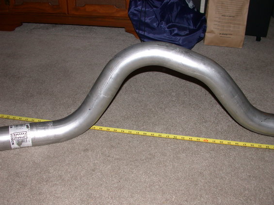Curved metal exhaust pipe with a yellow tape measure laid alongside it. Label reads M30001