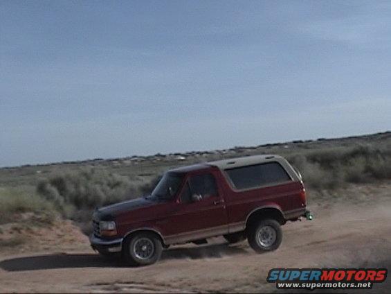 1994 Ford Bronco driving on a dirt road with brush and hills in background
