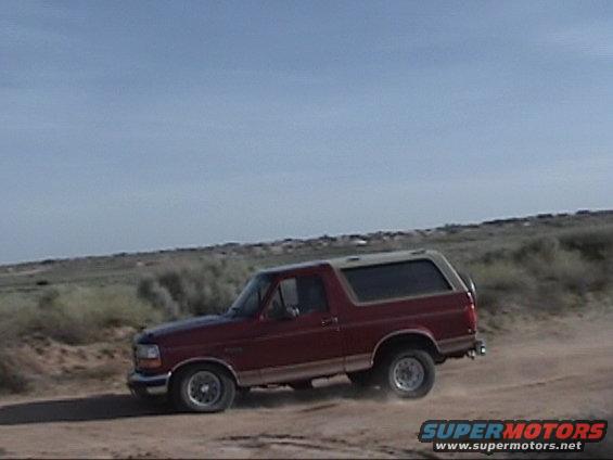 Red Ford Bronco with a tan top driving on a dirt road, kicking up dust