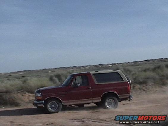 Red 1994 Ford Bronco driving on dirt road