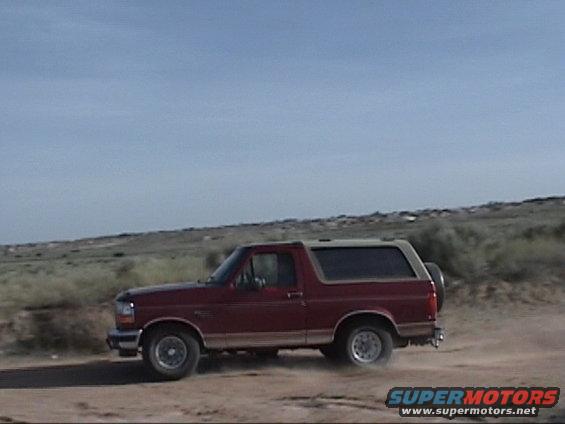 Red 1994 Ford Bronco driving on a dirt road with dust kicking up