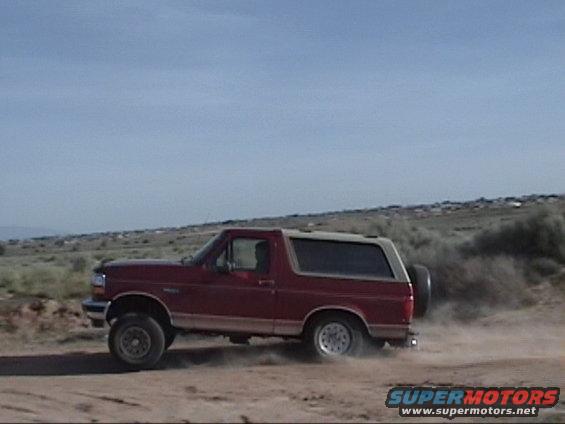 1994 Ford Bronco driving on a dirt road, kicking up dust. Side view