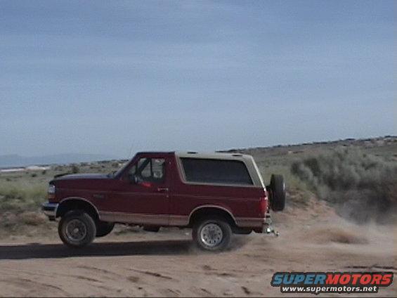 Red 1994 Ford Bronco side view, kicking up dust