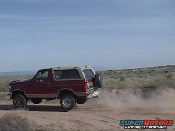 Red and tan Ford Bronco with a spare tire on the back, kicking up dust on a dirt road