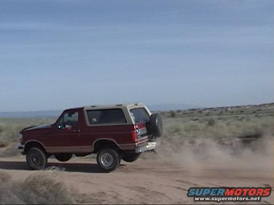 Red and tan 1994 Ford Bronco side view, kicking up dust