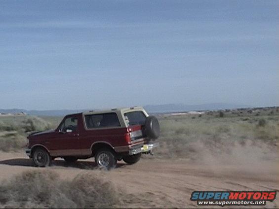 1994 Ford Bronco driving on a dirt road, rear-mounted spare tire visible