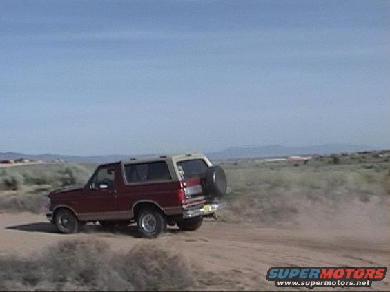 1994 Ford Bronco driving on a dirt road in a dry, open landscape