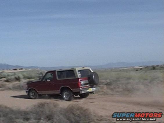 red SUV with spare tire on back driving on a dirt road in a dry, open landscape