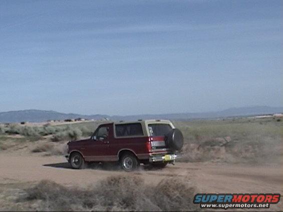 1994 Ford Bronco rear view, red and tan, driving on dirt road