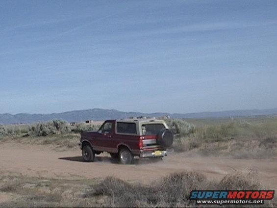 Red and tan Ford Bronco driving on a dirt road with mountains in the background