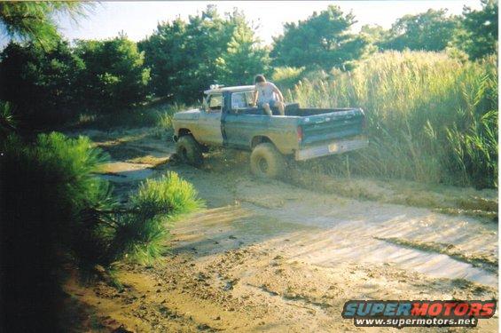 1979 Ford F-250 stuck in a muddy trail with a person sitting in the truck bed