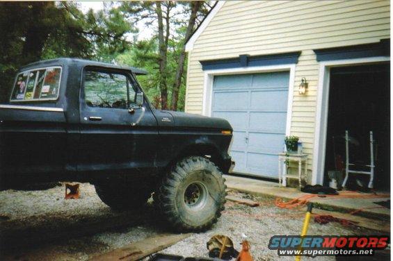1979 Ford F-250 pickup truck, black, lifted with large off-road tires, parked in driveway next to garage