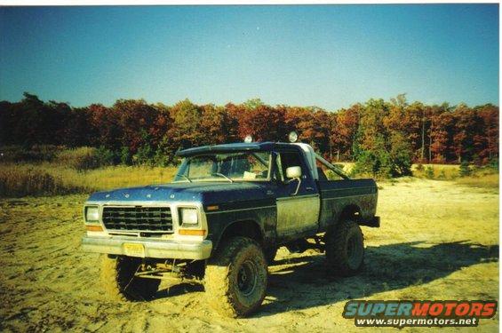 Blue 1979 Ford F-250 pickup truck with off-road tires and roll bar, parked on sandy terrain