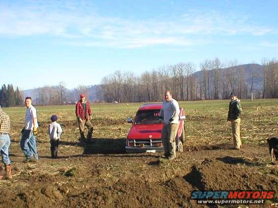 Red SUV stuck in mud with people standing nearby