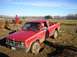 1978 Ford Bronco - A red pickup truck is stuck in a muddy field with a driver inside and another person standing nearby.