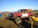 1978 Ford Bronco - A red 1978 Ford Bronco is stuck in the mud, with a driver visible behind the wheel and other people nearby.