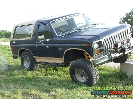 1986 Ford Bronco with aftermarket winch on front bumper, parked on grass with front right tire on a concrete block
