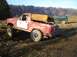 1978 Ford Bronco - A red Bronco with a tan soft top is driving through mud, with a green SUV in the background.