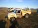1978 Ford Bronco - A white and orange 1978 Ford Bronco is stuck in the mud, its driver's side door ajar, while another off-road vehicle is visible in the back…