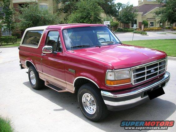Red 1995 Ford Bronco parked on a driveway, tan trim, chrome wheels, and a white roof