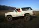 1978 Ford Bronco - A white Ford Bronco navigates a muddy terrain under a clear blue sky.