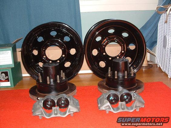Two black wheels with hubs and studs, two brake rotors, and two brake calipers arranged on a red mat