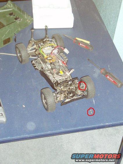 RC car chassis with exposed wires and suspension, next to screwdrivers and a green box