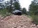 1978 Ford Bronco - 1978 Ford Bronco navigating a challenging off-road course in a wooded, rocky environment.