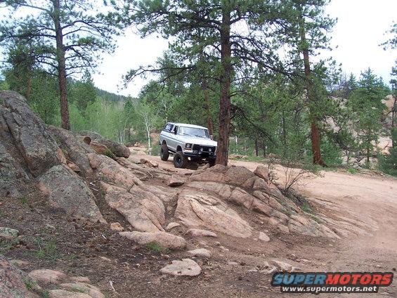 Silver 1978 Ford Bronco on a rocky, wooded trail