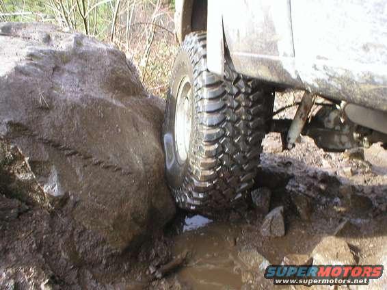 Off-road tire wedged against a large rock on a muddy trail