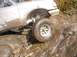1978 Ford Bronco - A silver pickup truck navigates a rocky, muddy terrain with water splashing.