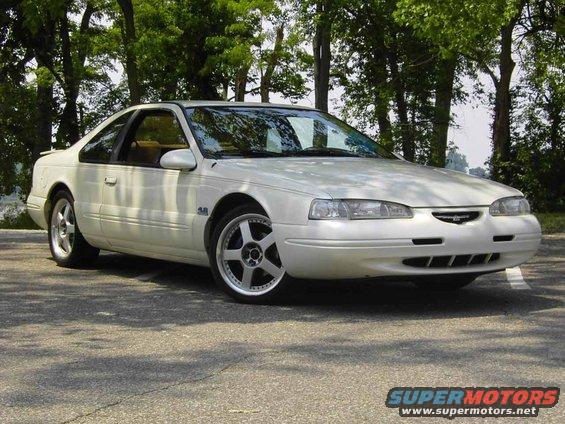 White 1996 Ford Thunderbird coupe parked on asphalt with trees in background