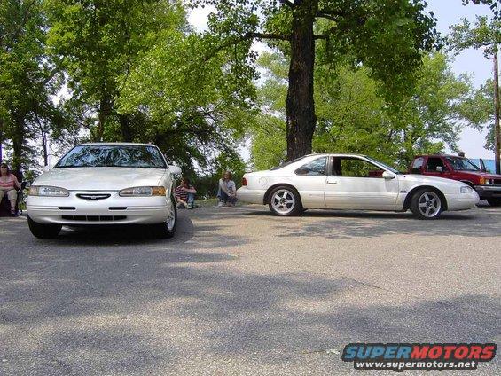 White Ford Thunderbird parked next to another car, with people sitting nearby