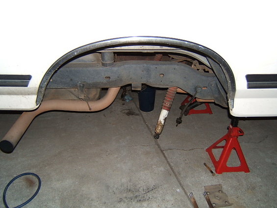 White vehicle's rear axle, leaf springs, and shock absorber removed and supported by jack stands