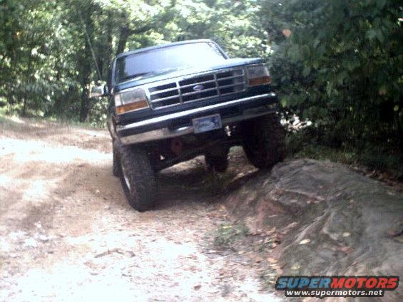 Green Ford Bronco climbing over a rock on a dirt trail
