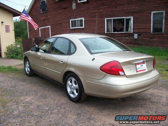 Gold 2000 Ford Taurus parked on gravel in front of a red barn with an American flag