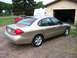 2000 Ford Taurus - A gold 2000 Ford Taurus sedan is parked in front of a garage, with a red sports car behind it.