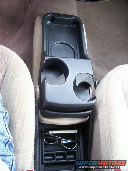 Car's center console with two cup holders, a storage bin, and a lower compartment holding sunglasses and a phone