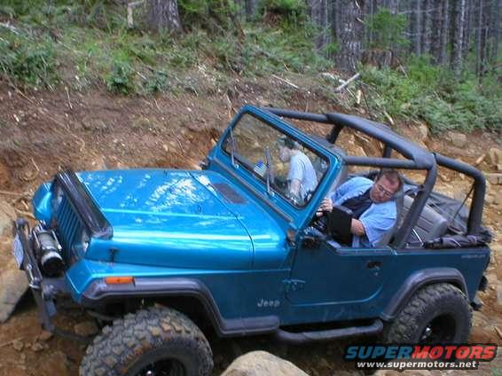 Blue Jeep Wrangler with roll cage off-roading on a dirt trail