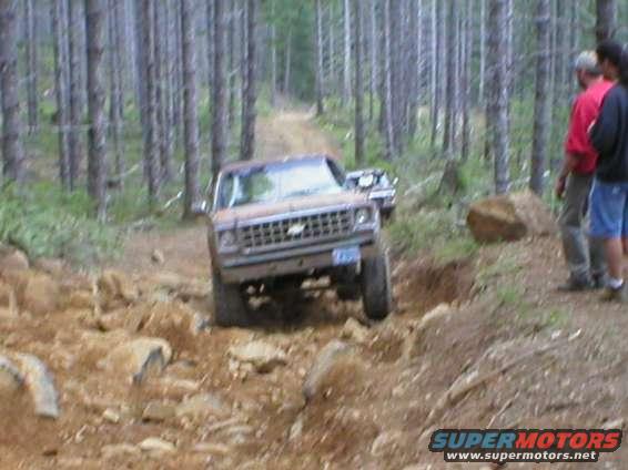 off-roading in a 1973 Chevrolet K5 Blazer on a rocky trail, another vehicle behind it