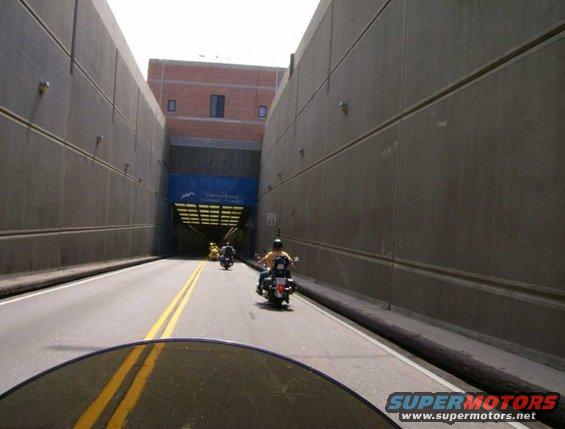 Motorcycles ride through a tunnel with a sign for the Chesapeake Channel Tunnel