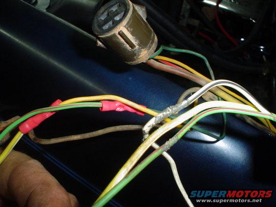 Close-up of a vehicle's wiring harness with several wires connected using red crimp connectors and silver tape. A brown electrical connector is visible at the top