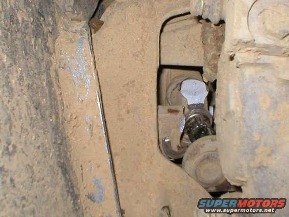 Close-up of a dirty, metallic vehicle undercarriage part with a bolt and hose