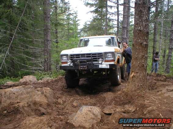 1978 Ford Bronco navigating a rocky, wooded trail. Driver is leaning on the door